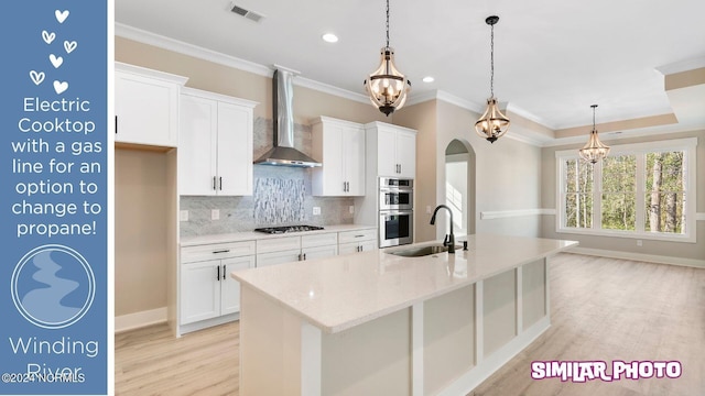 kitchen featuring white cabinets, sink, a kitchen island with sink, and wall chimney range hood