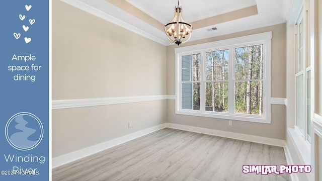 spare room featuring ornamental molding, light hardwood / wood-style floors, an inviting chandelier, and a tray ceiling