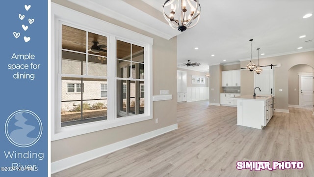 kitchen featuring a kitchen island with sink, white cabinets, sink, light hardwood / wood-style flooring, and decorative light fixtures