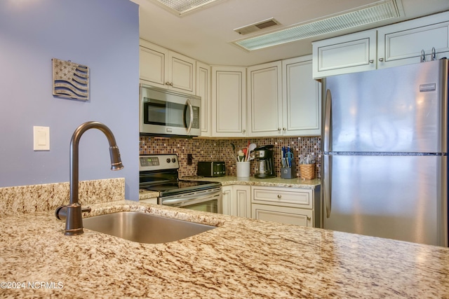 kitchen with backsplash, stainless steel appliances, sink, and light stone countertops