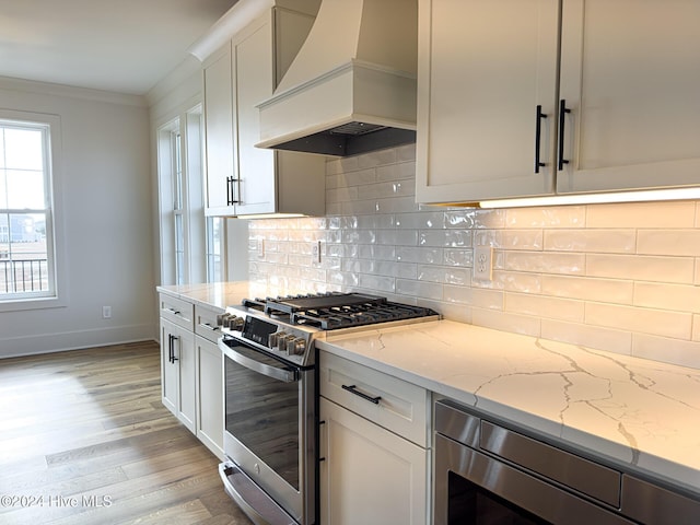 kitchen with white cabinets, light stone countertops, premium range hood, and high end stainless steel range