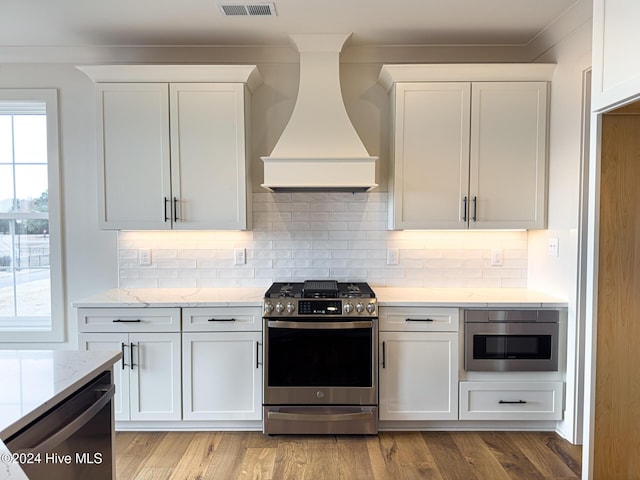 kitchen featuring dishwasher, stainless steel gas range oven, built in microwave, white cabinetry, and custom range hood