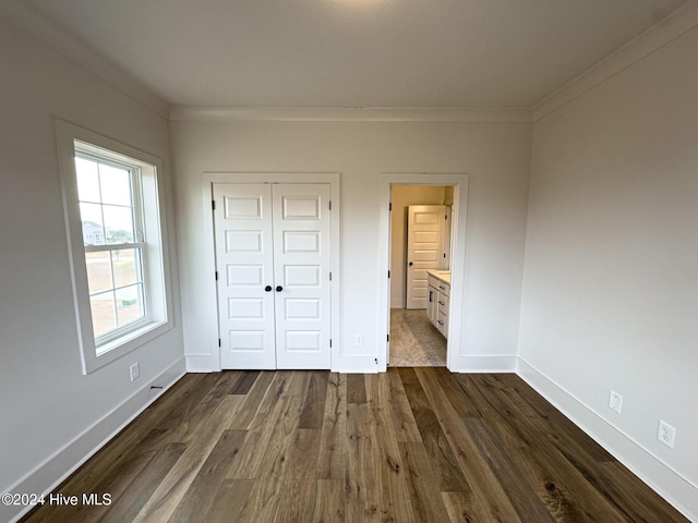 unfurnished bedroom with ensuite bath, a closet, dark wood-type flooring, and ornamental molding