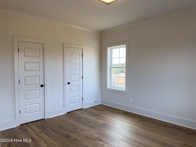 unfurnished bedroom with crown molding and dark wood-type flooring