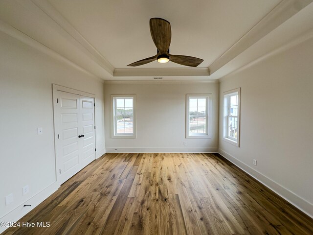 unfurnished bedroom with a tray ceiling, ceiling fan, a closet, and wood-type flooring