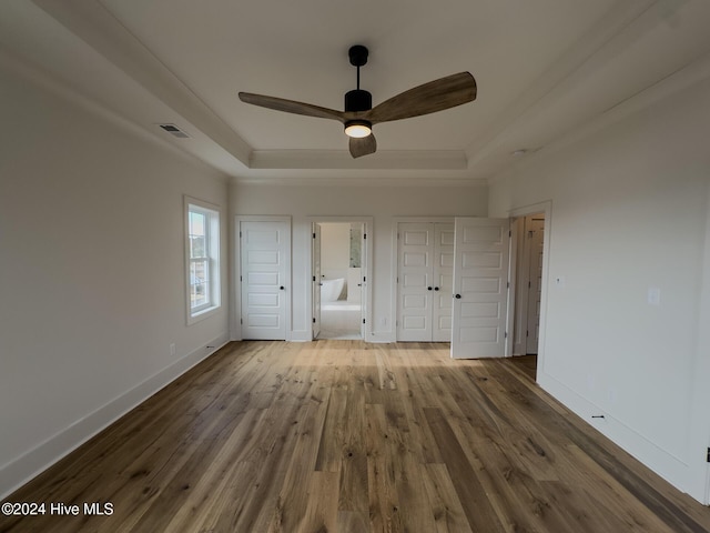 unfurnished bedroom featuring hardwood / wood-style flooring, a raised ceiling, ensuite bath, and ceiling fan