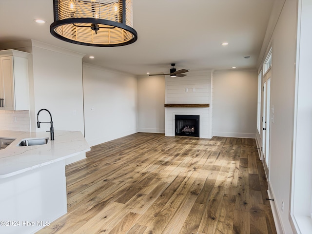 unfurnished living room featuring a large fireplace, ceiling fan, sink, and light hardwood / wood-style flooring