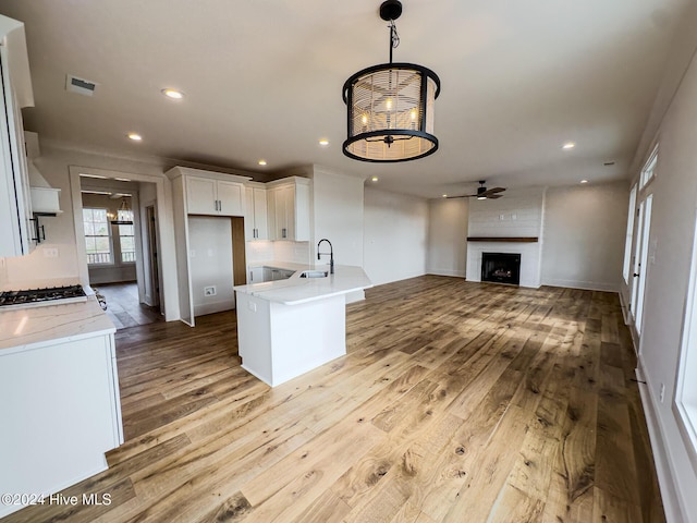 kitchen with white cabinets, sink, a brick fireplace, ceiling fan, and light wood-type flooring