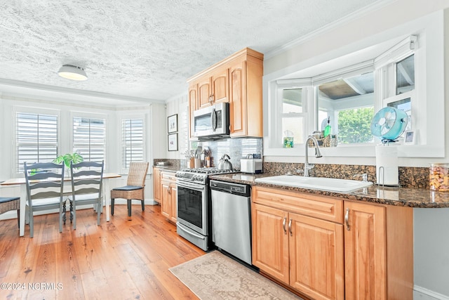 kitchen with dark stone counters, light hardwood / wood-style floors, crown molding, appliances with stainless steel finishes, and sink