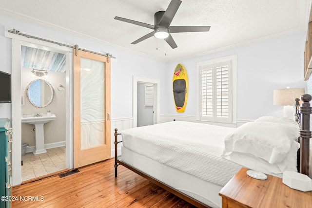 bedroom with ornamental molding, connected bathroom, hardwood / wood-style floors, a barn door, and ceiling fan