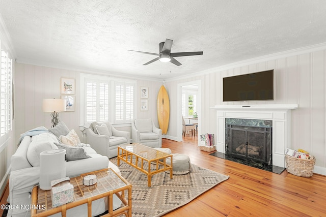 living room with crown molding, hardwood / wood-style flooring, ceiling fan, and a high end fireplace