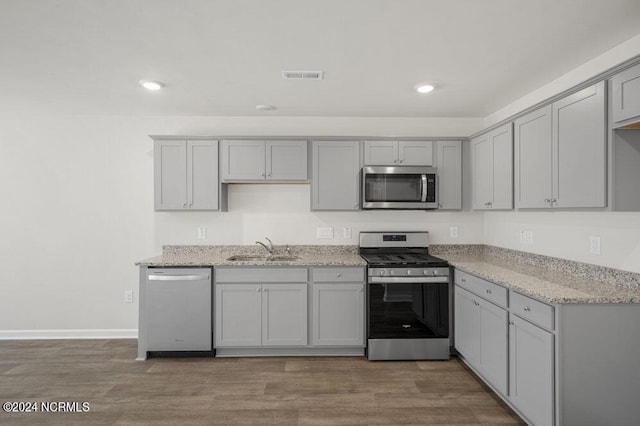 kitchen with gray cabinetry, sink, stainless steel appliances, light stone counters, and hardwood / wood-style floors