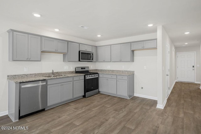 kitchen with light stone counters, stainless steel appliances, sink, light hardwood / wood-style flooring, and gray cabinets