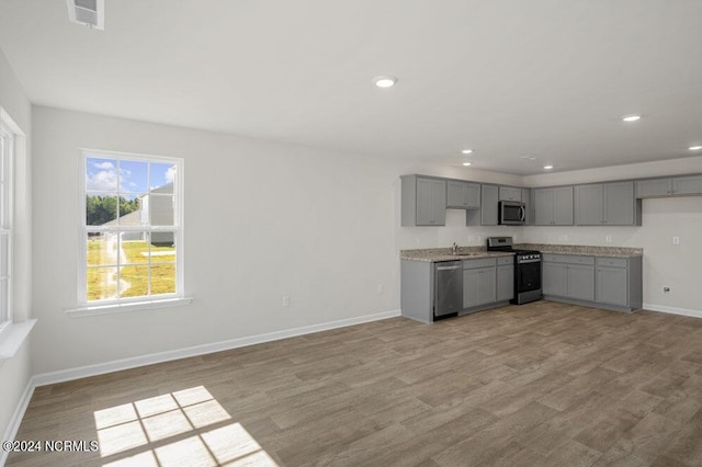 kitchen with appliances with stainless steel finishes, light wood-type flooring, gray cabinets, and sink