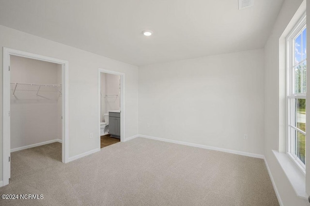 unfurnished bedroom featuring carpet flooring, ensuite bath, a spacious closet, and a closet