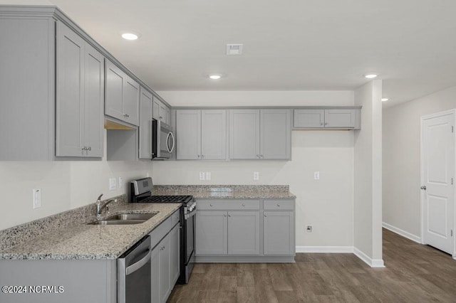 kitchen with gray cabinetry, sink, dark hardwood / wood-style floors, light stone countertops, and stainless steel appliances