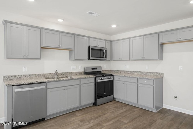 kitchen with gray cabinetry, sink, light hardwood / wood-style flooring, appliances with stainless steel finishes, and light stone counters