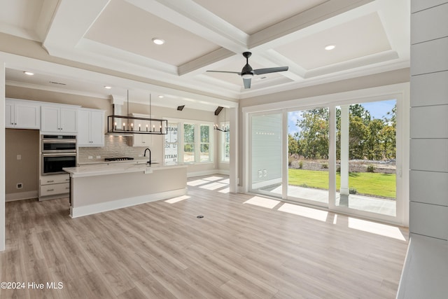 kitchen featuring white cabinetry, hanging light fixtures, an island with sink, double oven, and light hardwood / wood-style flooring