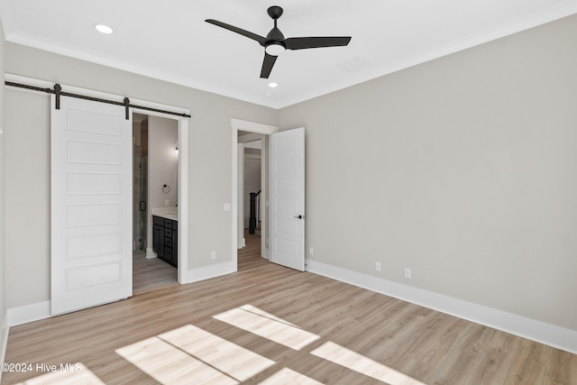 unfurnished bedroom with ceiling fan, a barn door, light hardwood / wood-style floors, and ensuite bathroom