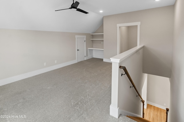 interior space with built in features, ceiling fan, light carpet, and vaulted ceiling