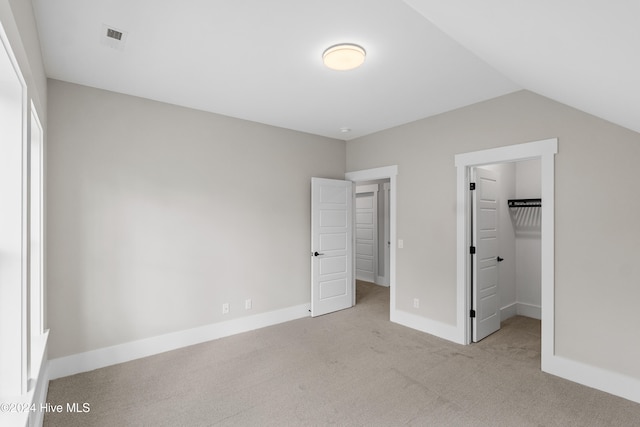 unfurnished bedroom with a closet, a walk in closet, vaulted ceiling, and light carpet