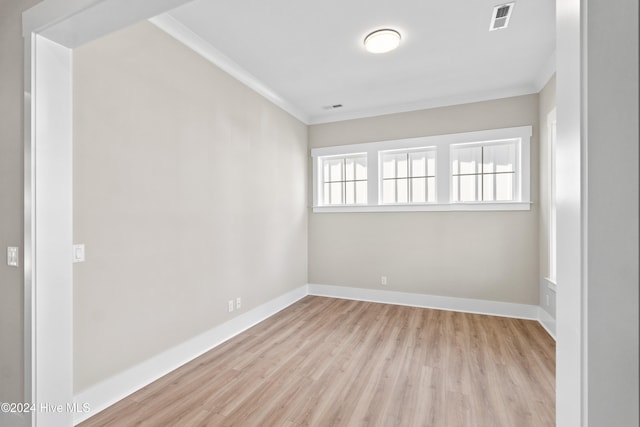 empty room featuring light wood-type flooring, a wealth of natural light, and crown molding