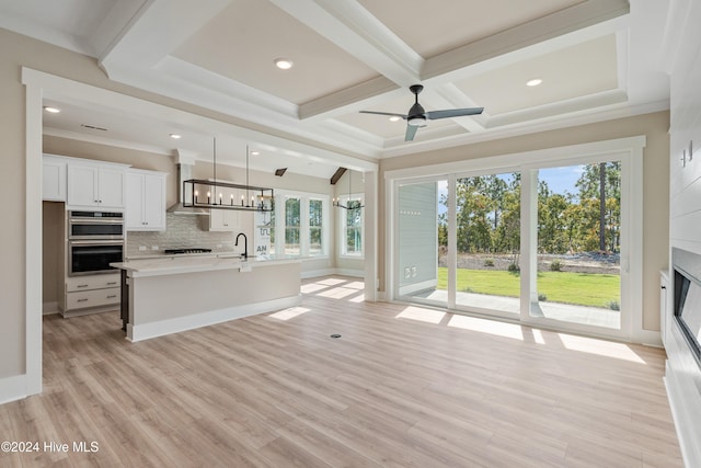 unfurnished living room featuring a wealth of natural light, ceiling fan with notable chandelier, and light hardwood / wood-style floors