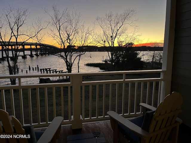 balcony at dusk featuring a water view