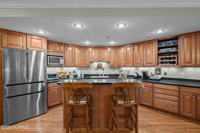 kitchen featuring appliances with stainless steel finishes, light wood-type flooring, a kitchen breakfast bar, ornamental molding, and a kitchen island