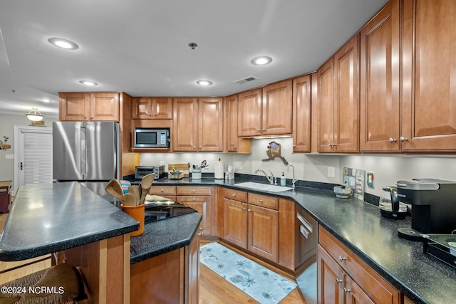 kitchen with sink, a center island, a breakfast bar, appliances with stainless steel finishes, and light wood-type flooring