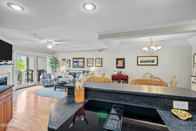 living room featuring ceiling fan with notable chandelier, ornamental molding, a tile fireplace, and light hardwood / wood-style flooring