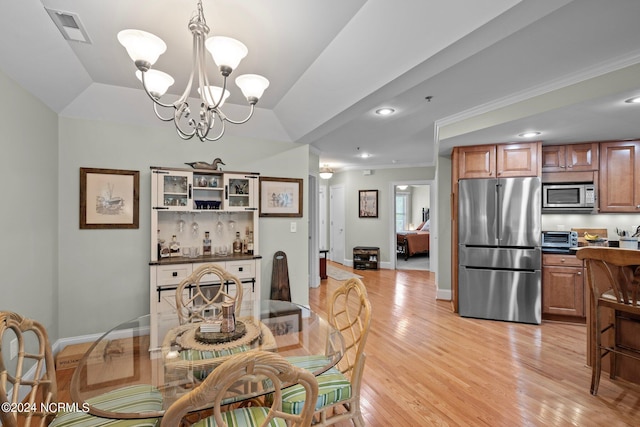 dining room with a notable chandelier, light hardwood / wood-style floors, lofted ceiling, and ornamental molding