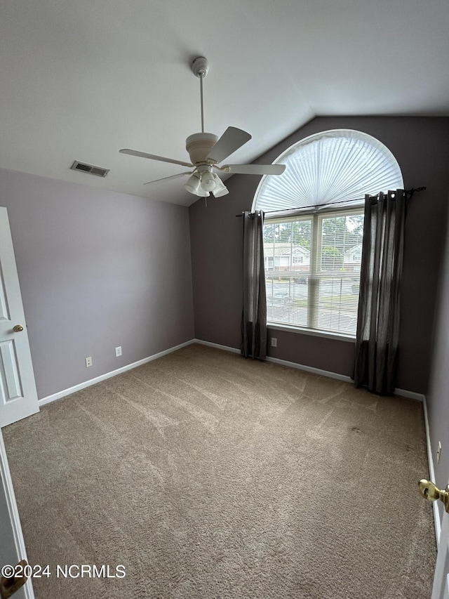 empty room featuring carpet floors, visible vents, vaulted ceiling, and ceiling fan