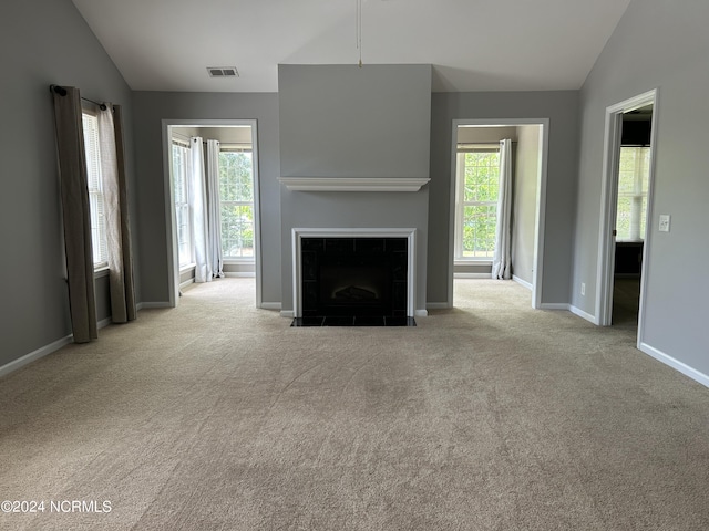 unfurnished living room featuring a tile fireplace, a healthy amount of sunlight, and vaulted ceiling