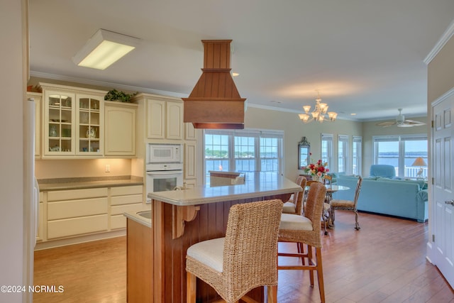 kitchen with white appliances, cream cabinets, ceiling fan with notable chandelier, light wood-type flooring, and a healthy amount of sunlight