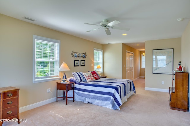 bedroom featuring multiple windows, ceiling fan, a closet, and light carpet