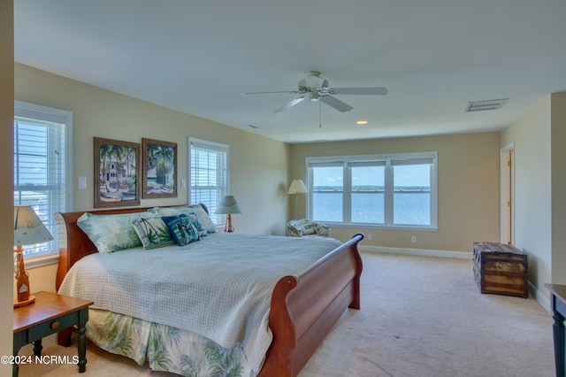 bedroom with light carpet, a water view, and ceiling fan