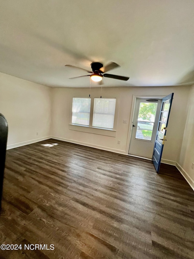 empty room featuring dark wood finished floors, a ceiling fan, and baseboards