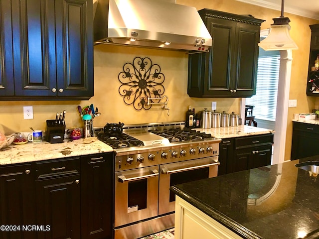 kitchen with dark stone countertops, ornamental molding, wall chimney exhaust hood, and range with two ovens