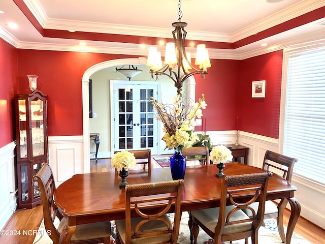 dining area featuring ornamental molding, an inviting chandelier, french doors, a raised ceiling, and light hardwood / wood-style floors