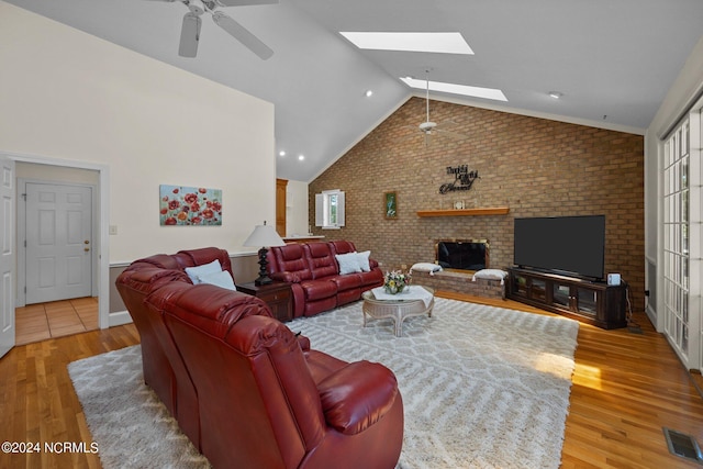 living room featuring ceiling fan, brick wall, lofted ceiling with skylight, and light hardwood / wood-style floors