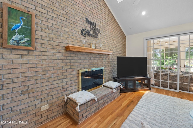 living room featuring a brick fireplace, high vaulted ceiling, brick wall, and light wood-type flooring