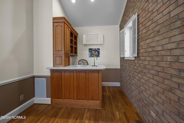 kitchen featuring lofted ceiling, dark hardwood / wood-style floors, kitchen peninsula, and brick wall