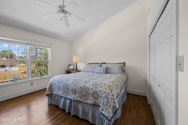 bedroom featuring dark wood-type flooring, vaulted ceiling, a textured ceiling, a closet, and ceiling fan