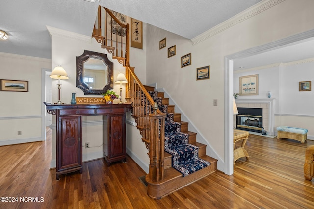 stairs featuring a textured ceiling, a tiled fireplace, wood-type flooring, and ornamental molding