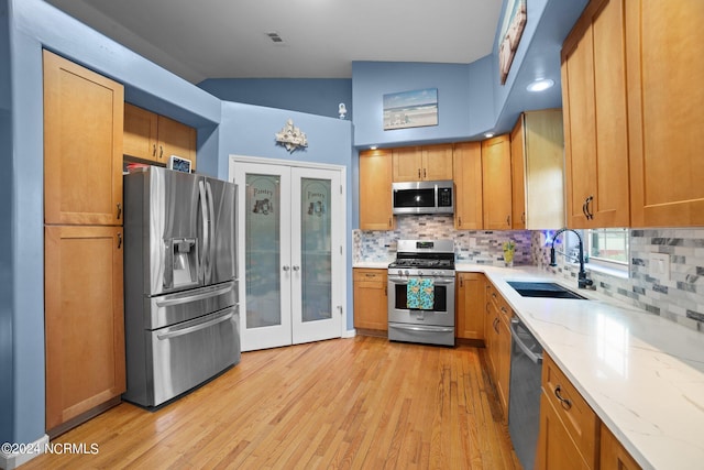 kitchen with light stone counters, stainless steel appliances, a sink, and french doors