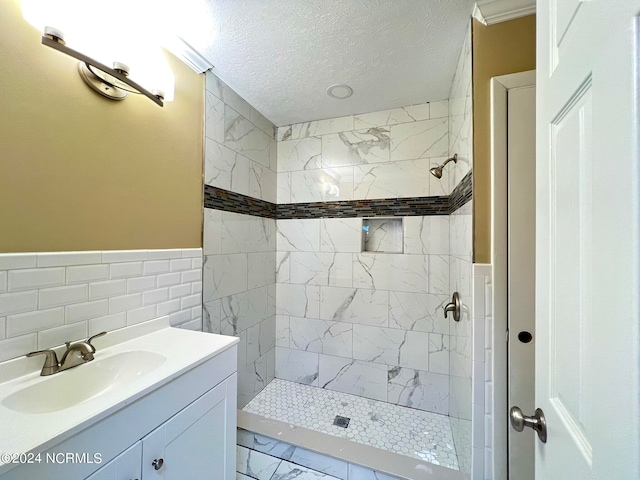 bathroom featuring a tile shower, a textured ceiling, vanity, and tile walls