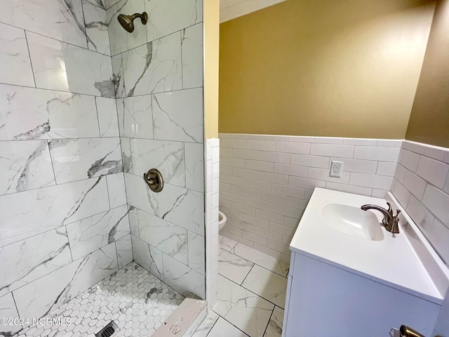 bathroom featuring a tile shower, vanity, toilet, and tile walls