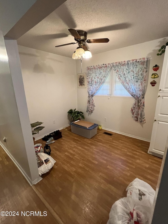 interior space with a textured ceiling, hardwood / wood-style flooring, and ceiling fan