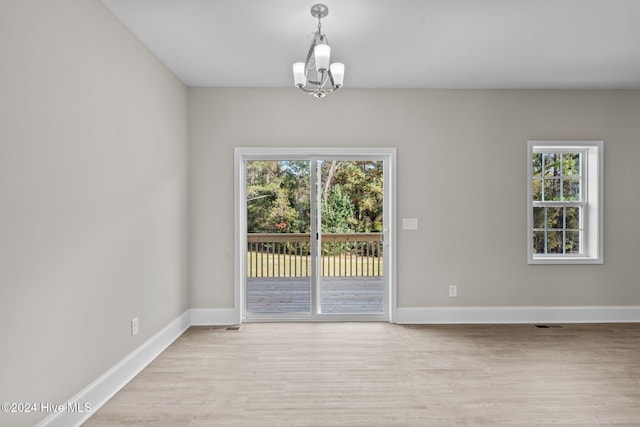 unfurnished room featuring light wood-type flooring, a healthy amount of sunlight, and an inviting chandelier